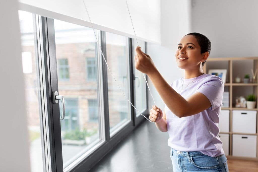 A woman smiles while pulling the blinds over her casement windows